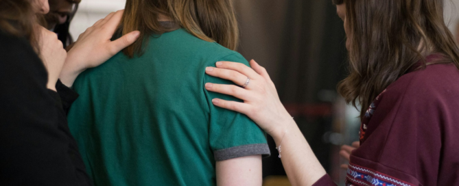 Three women placing supportive hands on another woman's shoulders in a group setting